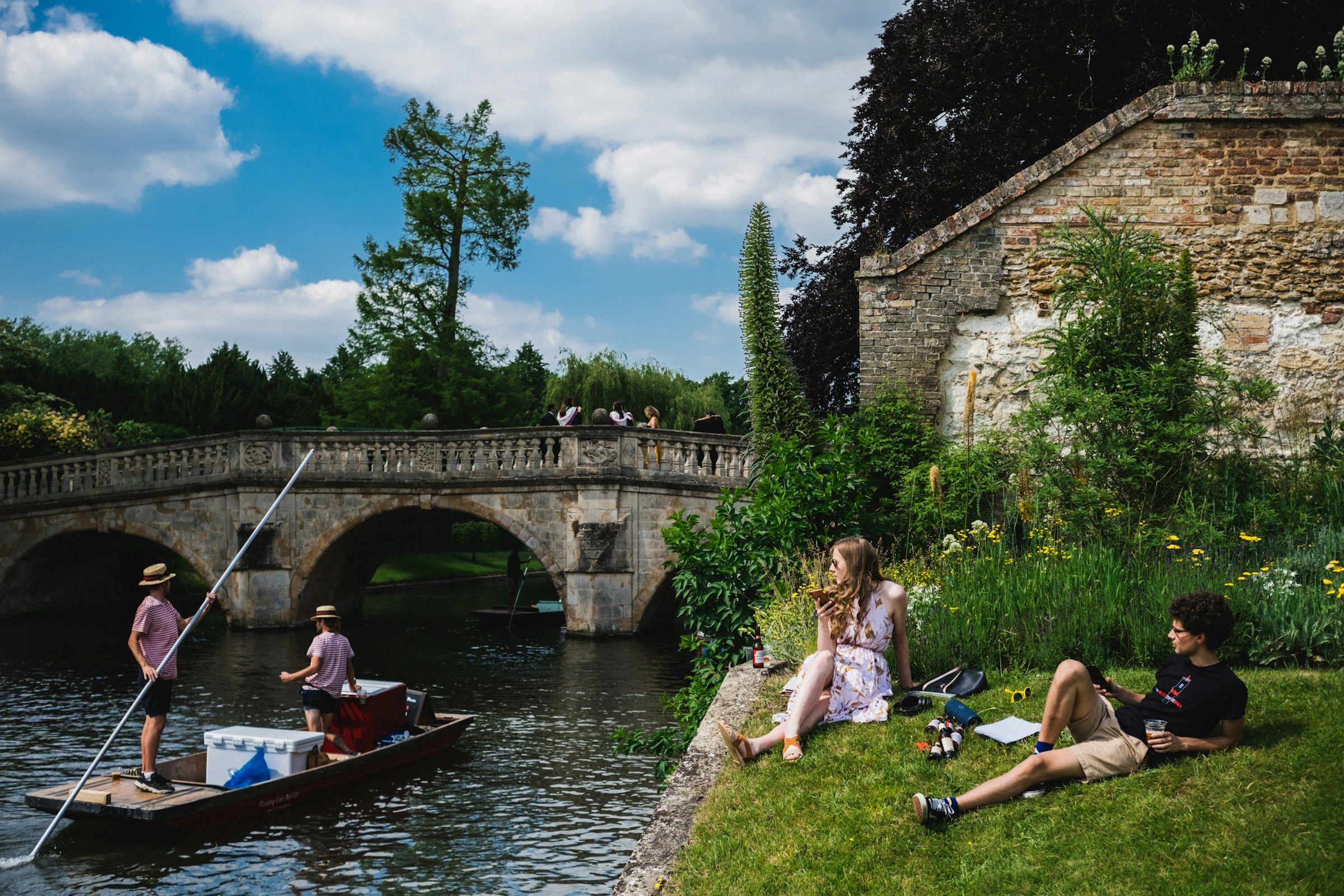 Cambridge’de nehir kenarında çimlere oturmuş öğrenciler ve kayıkla gezenler